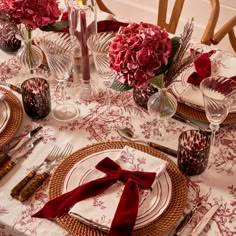 the table is set with red flowers and silverware