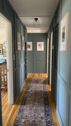 a long hallway with blue walls and wooden flooring, framed pictures on the wall