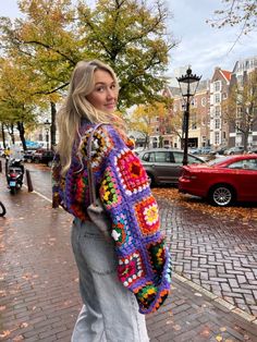 a woman is walking down the street wearing a colorful crochet jacket and jeans