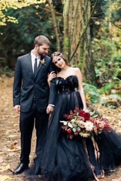 a man and woman in formal wear standing next to each other on a forest path