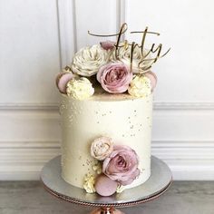 a white and pink wedding cake with flowers on top is sitting on a silver plate