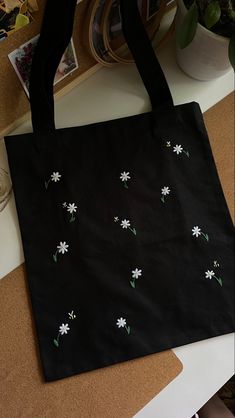 a black bag with white flowers on it sitting on top of a table next to a plant