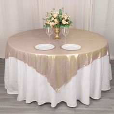 a table with two white plates and flowers on it, sitting in front of a curtain