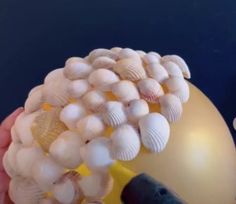 a person holding a yellow balloon with seashells on it's side and an object in the background