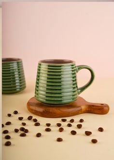 two green mugs sitting on top of a wooden spoon next to some coffee beans