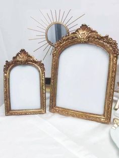 two gold framed mirrors sitting on top of a table