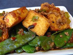 a white plate topped with fried tofu and green beans on top of leafy greens