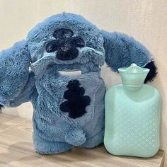 a blue stuffed animal sitting next to a bottle on a shelf with a white wall in the background