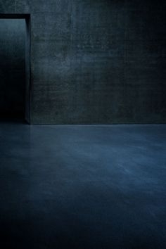 an empty room with dark walls and concrete flooring is lit by a single light