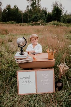 a little boy sitting at a desk in the middle of a field with writing on it