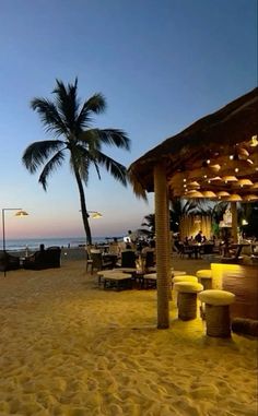 the beach is lined with tables and chairs under palm trees at dusk on a tropical island