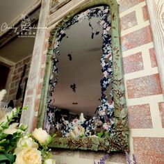 a mirror with flowers in front of it sitting on a wall next to a window