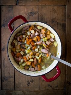 a pot filled with meat and vegetables on top of a wooden table