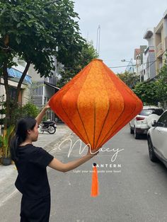 a woman holding up an orange kite on the street