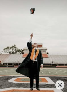 a man in a graduation gown and orange scarf flying a kite on the football field