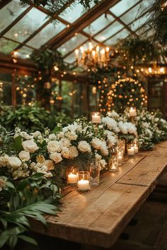 a long table with candles and flowers in vases on it, surrounded by greenery