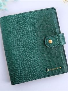 a green leather notebook with a gold button on the front and side, sitting on a white surface