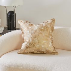 a white chair with a gold pillow on it and a lamp in the corner behind it