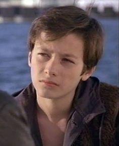 a young man sitting next to the water with his eyes closed and looking off into the distance