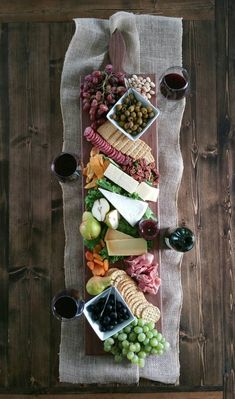 a wooden platter filled with different types of cheese and meats next to two glasses of wine