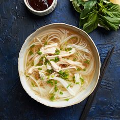 a bowl of chicken noodle soup with chopsticks and sauce on the side