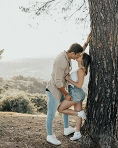 a man and woman kissing next to a tree