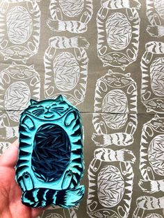 a hand holding a small blue object in front of a wall with designs on it