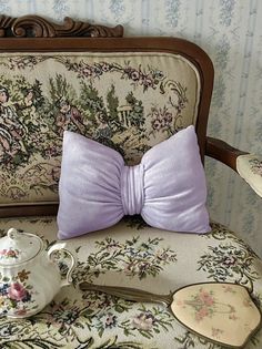 a purple bow tie sitting on top of a chair next to a tea pot and spoon