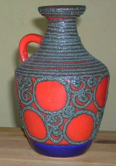 an orange and blue vase sitting on top of a wooden table