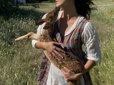 a woman holding a baby deer in her arms while standing in the middle of a field