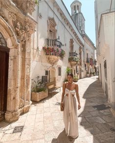 a woman is walking down the street in an old european town, wearing a white dress