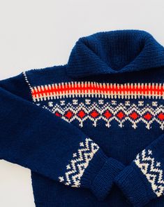 a blue sweater with red and white designs on the collar is sitting on a white surface