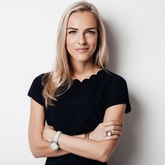 a woman with her arms crossed standing in front of a white wall and looking at the camera