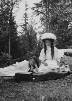 an old photo of two women sitting on a blanket in the woods with one woman laying down