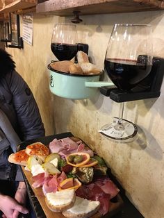 a person holding a tray with food and wine on it in front of a wall