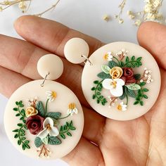 two white earrings with flowers on them are being held in someone's hand,