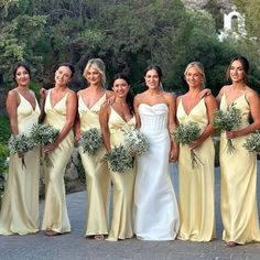 a group of women standing next to each other wearing dresses and holding bouquets in their hands