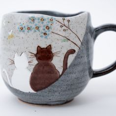 This elegant Japanese mug cup is part of the cherished 'Cats in Sunny Spot' collection, celebrated for its charming depiction of two cuddling cats. Fashioned from textured stoneware in serene tones of blue and white, this cup exudes a warm and authentic ambiance. Skillfully shaped on a potter's wheel, it offers a comforting sensation when cradled. Its substantial thickness ensures beverages retain their warmth, making it an ideal companion during colder seasons. Additionally, it's a perfect gift Cats Cuddling, Cat Coffee Cups, Spotted Cat, Japan Gifts, Japanese Colors, Hand Painted Cat, Cat Cuddle, Kitty Stuff, Matcha Bowl