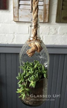 a hanging planter filled with succulents in a glass jar next to a brick wall