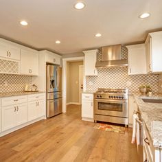 a large kitchen with white cabinets and stainless steel appliances, wood flooring and marble counter tops