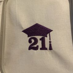 embroidered graduation cap with the number 21 on it in purple and white linen, sitting on top of a suitcase