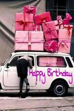 a white car with pink presents on the top and purple lettering that says happy birthday