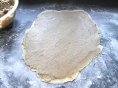 an uncooked pizza dough on a baking sheet next to a bowl of flour