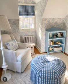 a blue and white living room with an ottoman, chair, bookcase and window