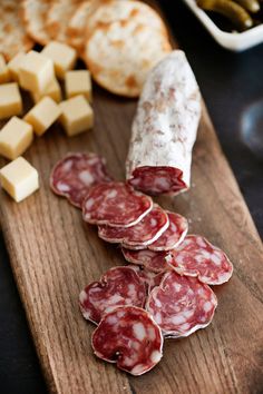 several slices of salami on a cutting board with cheese and olives in the background