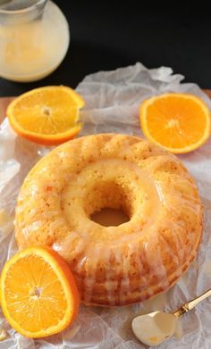 an orange bunt cake with icing and sliced oranges on the table next to it