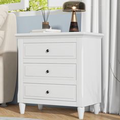 a white night stand with three drawers and a lamp on the end table next to it