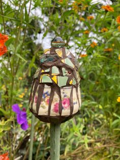 a bird feeder sitting on top of a wooden pole in front of some colorful flowers