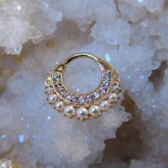 a gold nose ring with white pearls on top of some crystal rocks and ice crystals