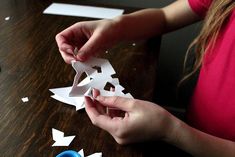 a person cutting out pieces of paper on a table with scissors and other crafting supplies